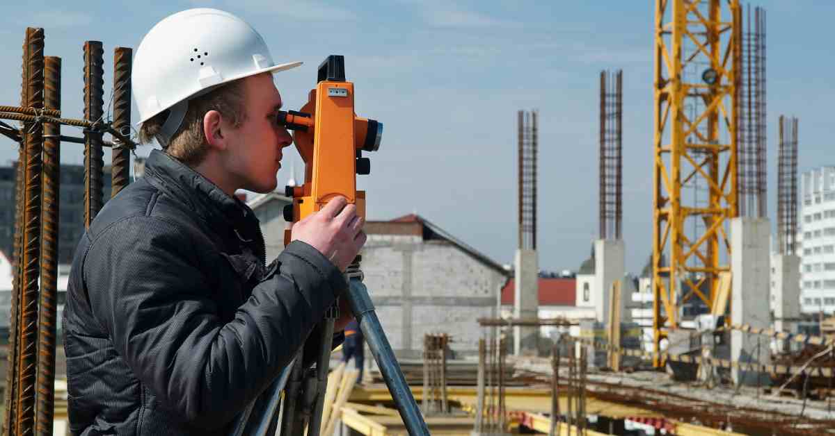 A professional at a construction site using 3D scanning equipment. He is wearing a hard hat and winter coat.